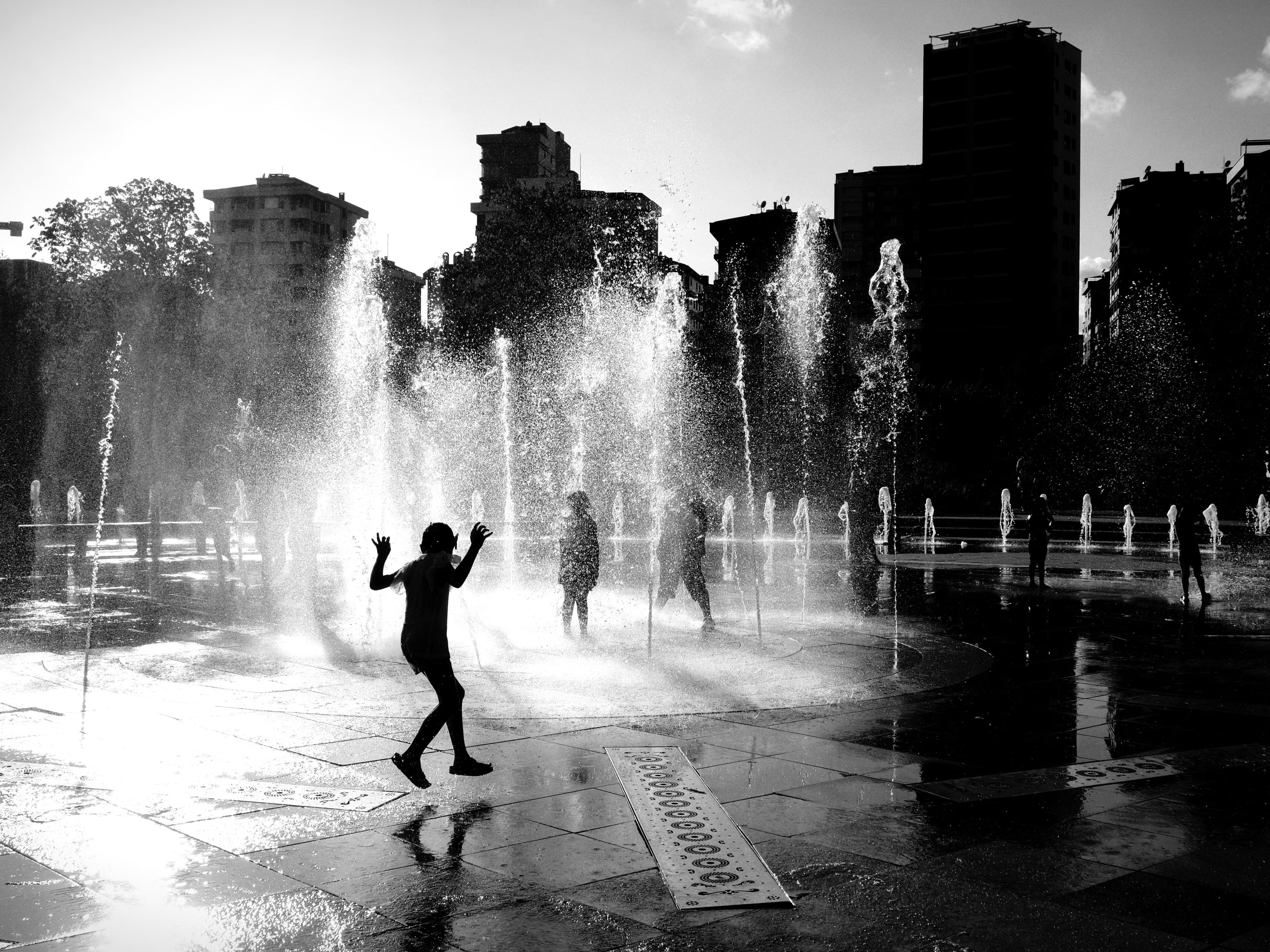 Black-and-white photo of children playing at an urban splash pad