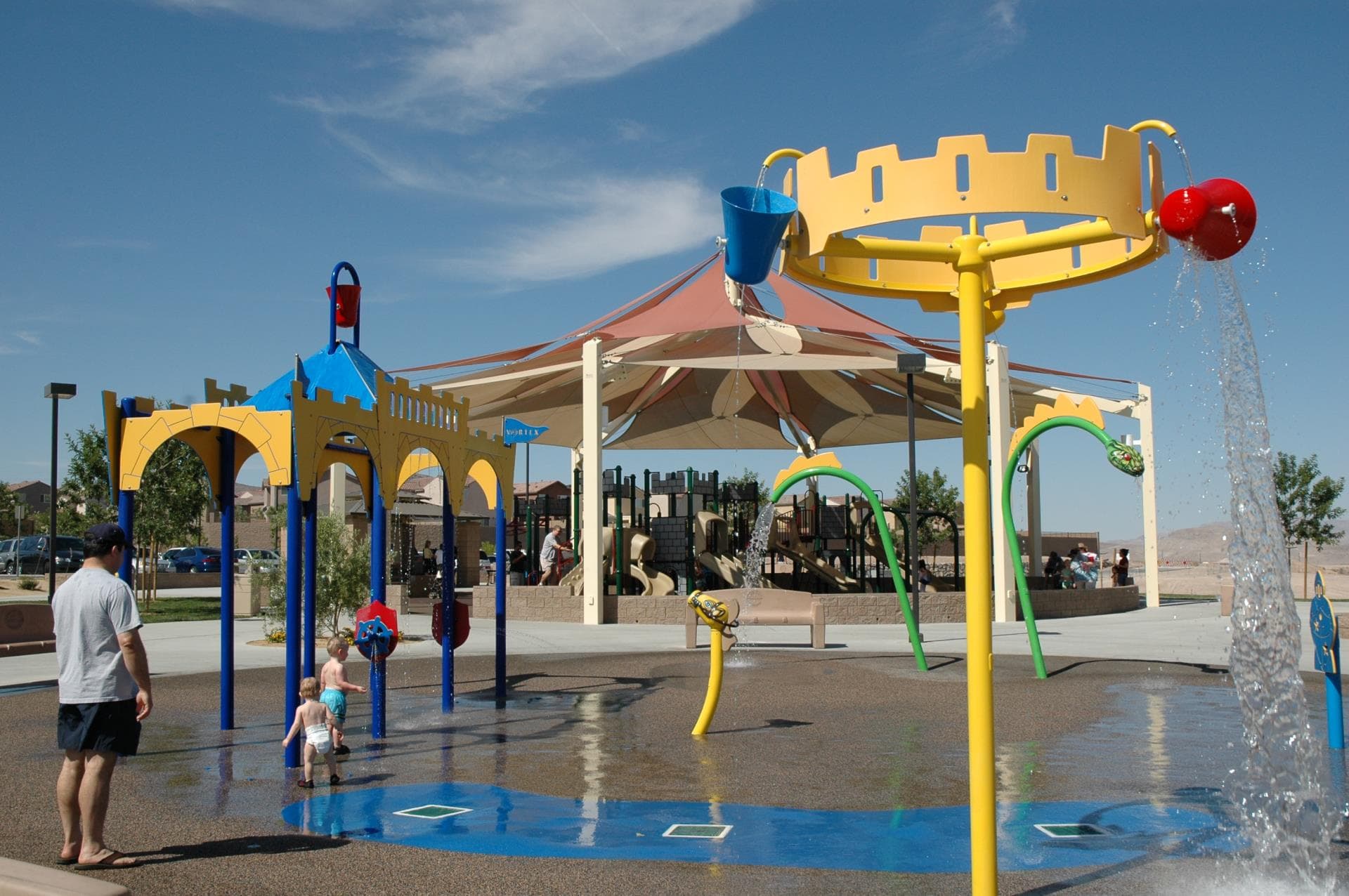 A father watches two toddlers play at a castle-themed splash pad in Henderson, Nevada